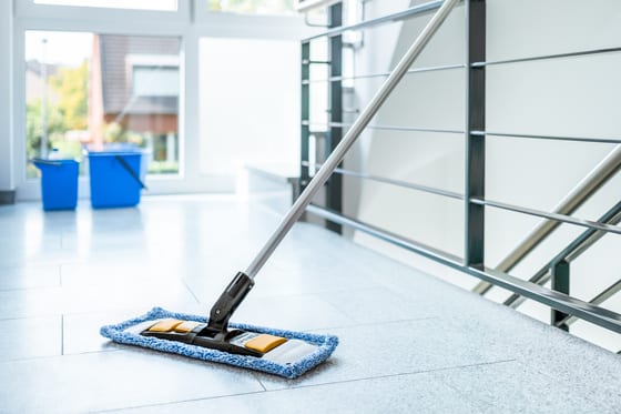 Nettoyage Professionnel des Sols : Moppe et Seaux Moppe professionnelle sur carrelage gris avec seaux bleus en arrière-plan près d'un escalier moderne.